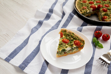 A Piece of Homemade Spinach Quiche on a white plate, side view. Copy space.