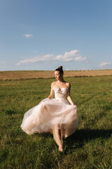 Fototapeta na wymiar Fashion posing of gorgeous bride. Elegant bride walking in field in wedding dress