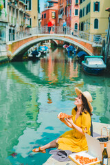 Fototapeta na wymiar woman sitting on pond with view of venice canal eating pizza