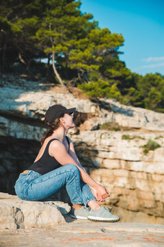 young pretty woman sitting on the cliff looking at sea