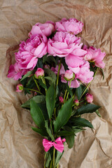 Fluffy bouquet of pink peonies flowers in sunlight on wrinkled craft paper background