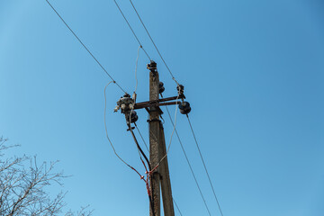 Power line post with electricity cables against a clear sky with white clouds. A tree grows near a...