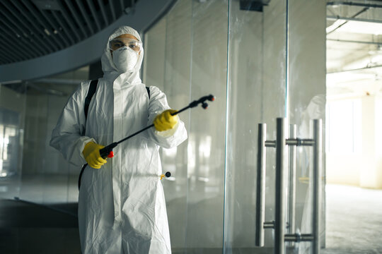 Sanitary worker sprays an empty business center with antiseptical liquid to prevent covid-19 spread. A man wearing disinfection suit cleaning up the shopping mall. Nobody, health, isolated concept.