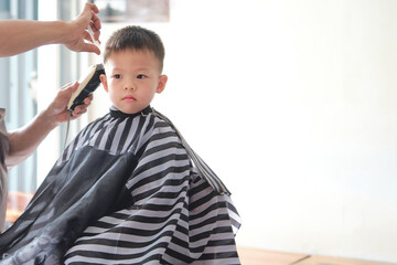 Cute little Asian 4 - 5 years old kindergarten boy child getting a haircut at the hairdresser's barber shop, Kid cut with hairdresser's machine with copy space on the right side