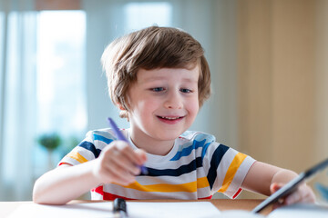 Back to school. Distance learning online education. Caucasian smile kid boy studying at home with smartphone and doing school homework. Smiling child siting at table with cell phone