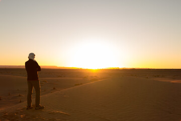 A man alone in a turban with his arms crossed watches the sunrise in the Erg Chebbi desert in Merzouga, Morocco