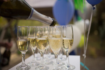 Somebody pouring champagne into glasses on terrace on the table. Party