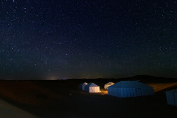 Fototapeta na wymiar Illuminated tents from a camp in the Erg Chebbi desert in Merzouga, under a spectacular starry sky in Morocco