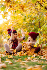 girls in the hat sit in autumn Park with maple leaf  and play, have fun.