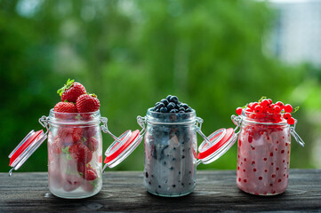 Banks with summer berries on a black wooden window sill. Strawberries, currants and blueberries in cans in nature.