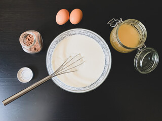 The process of preparing a dessert on a black wooden table. Flour, eggs, milk, honey, cocoa and a...