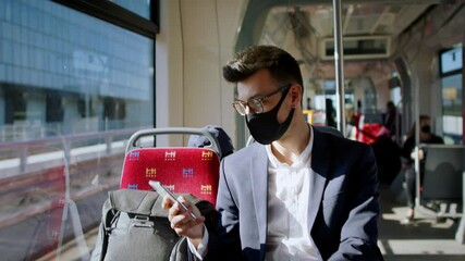 Portrait of young businessman with face mask sitting in public transport, travelling to work. - Powered by Adobe