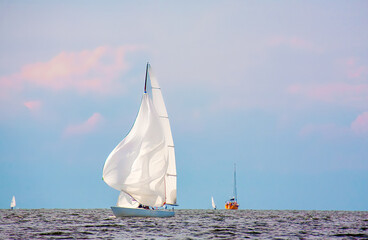 Yacht with a large sail - a spinnaker floats on the sea against a blue sky with clouds, yachtsport...