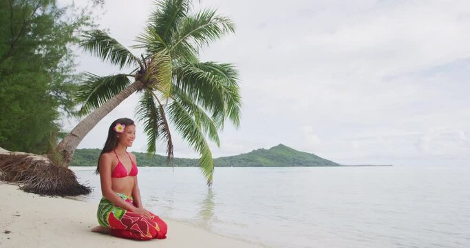 Beach woman relaxing on Bora Bora Tahiti island under the sun wearing polynesian skirt and monoi flower with palm tree background. Polynesia culture travel concept.