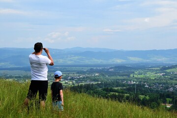 Unidentified father and son are standing in the high grass of the meadow and looking at Bialka...