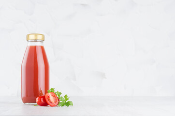 Fresh red tomato juice in glass bottle  template with green parsley, vegetables slices on wood table and white background with copy space.