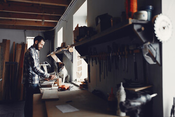 A man carves a tree. The carpenter works in a studio. Boy with cute dog