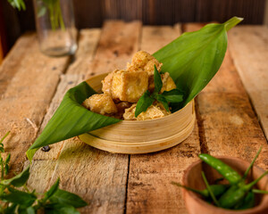 fried tahu or soybean cake served on banana leaf and woven bamboo tray, complete with chili and basil leaves on the wooden table