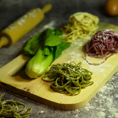 raw green, red and yellow vegetarian rainbow noodles with pak choi on wooden base, completed with eggs and wooden rolling pin isolated on gray dark or black