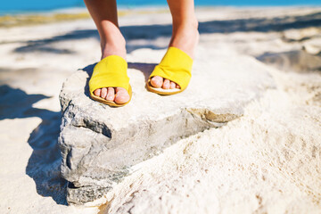 legs in yellow shoes on stone on white sandy beach