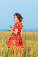 Portrait of a beautiful young woman   in red romantic dress with yellow flowers walking on the field , enjoying the day, on a sunny summer day. 