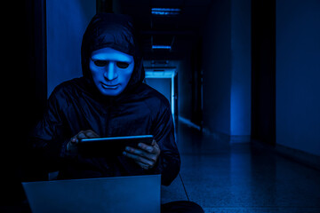 Anonymous computer hacker in white mask and hoodie. Obscured dark face working on her labtop and...