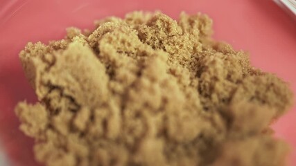Close-up brown sugar in a transparent glass bowl in 4K. A bunch of brown sugar on a pink background - Powered by Adobe