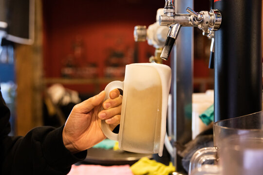 Hand pouring a fresh foamy frozen glass of beer at the restaurant.