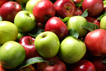 Pile of tasty ripe apples with leaves as background, closeup