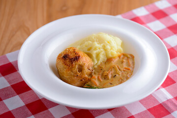 Traditional cuisine, mashed potatoes with gravy, meat and dill served on a white plate on a plaid background
