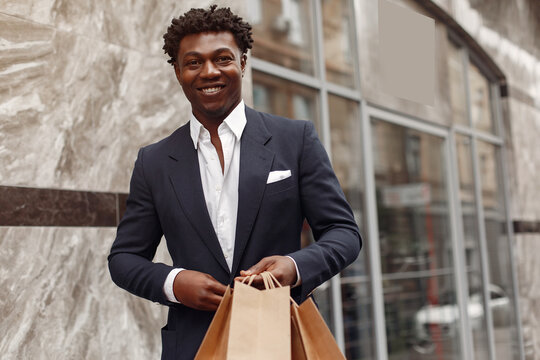 Black man in a city. Guy with shopping bags. Man in a black suit;