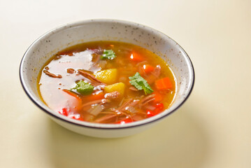 Delicious stew soup with meat and vegetables served in a white bowl over bright pastel yellow background. Healthy diet.