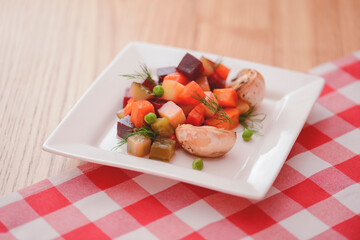 Steamed vegetables salad served on a square white plate on rustic wooden table with red plaid tablecloth.