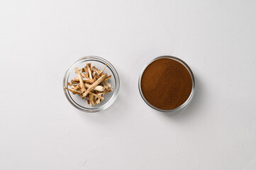 A healthy drink, an alternative to coffee. Dried roots and dry chicory powder in two glass bowls. Light gray concrete background. Top view, space for text.