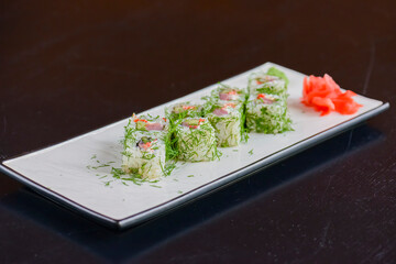 Salmon sushi rolls served on a white plate with ginger and wasabi and soy sauce in a restaurant table. Japanese cuisine.