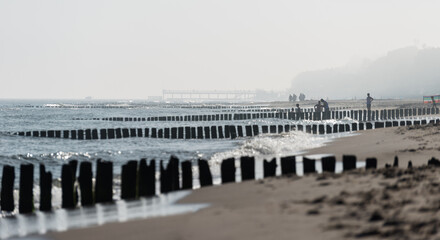 Fototapeta na wymiar Misty morning on the Polish beach visible people, sea, screens and wooden breakwaters.