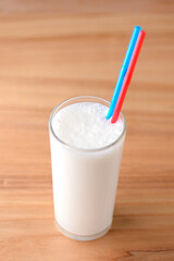 Vanilla milkshake in a tall galss with two plastic straws on light rustic wooden table.