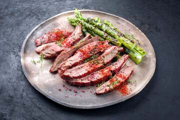 Traditionelles gegrilltes dry aged Wagyu Flanksteak aufgeschnitten und angeboten mit grünen Spargel und Chili als close-up auf einem rustikalen Modern Design Teller