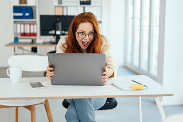 Excited young businesswoman staring at her laptop