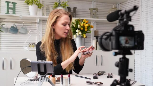 Beauty blogger woman filming daily make-up routine tutorial near camera. Influencer girl live streaming cosmetics product review. Vlogger female recommends eye shadow palette, teaches in masterclass.