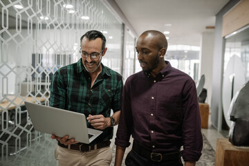 Two businessmen walking in an office an working on a laptop