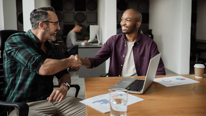 Two smiling diverse businessmen shaking hands in an office