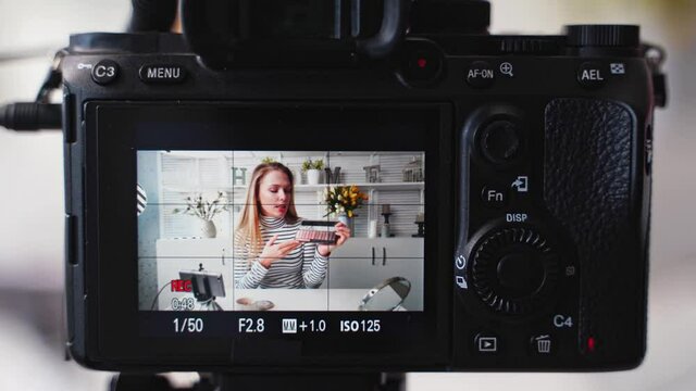 Camera screen recording - vlogger female shows eye shadow palette. Beauty blogger woman filming make-up tutorial at camera. Influencer blonde girl live streaming cosmetics product comparison in studio