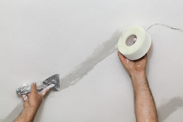 Worker fixing cracks on ceiling, spreading plaster with trowel over fiber mesh