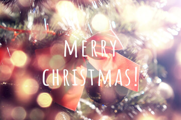 Christmas background with lettering 'Merry Christmas'. Back soft light. Decorations on the christmas tree, red bow, garland lights. Beautiful golden bokeh.