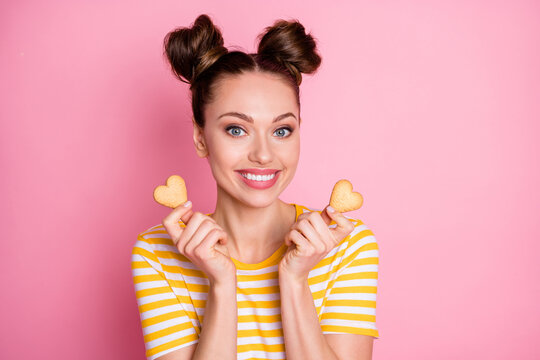 Closeup photo of attractive funny cheerful lady two buns hold hands heart shaped cookies sugar addicted yummy wear casual white yellow striped shirt isolated pink color background