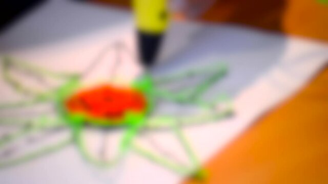 Blurred background. The man paints a flower 3d-pen close-up