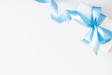 White gift box with blue ribbon on white background. Christmas, Birthday and New year concept. Flat lay, top view, copy space.