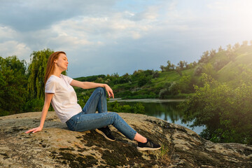 Naklejka na ściany i meble Relaxation, meditation, Digital detox, wellbeing, mental health concept. Red-haired woman meditates and relaxes in nature outdoor rocks at sunset.