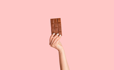 Millennial woman holding bar of organic chocolate over pink background, close up of hand